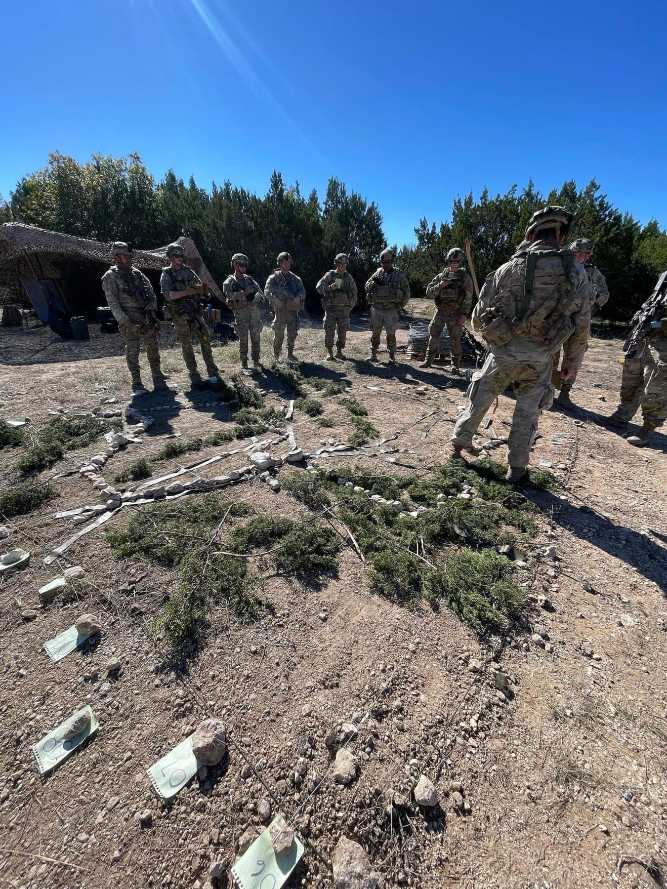 Joey LeBlanc in uniform briefing a group of soldiers in uniform during a field training exercise.